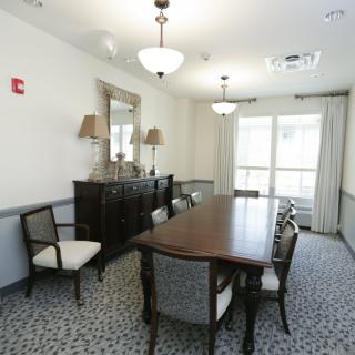 A well-lit dining room with a long wooden table, upholstered chairs, and elegant decor.