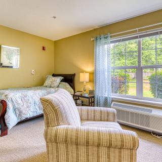 A cozy bedroom with a bed, armchair, and a large window allowing natural light to fill the room.