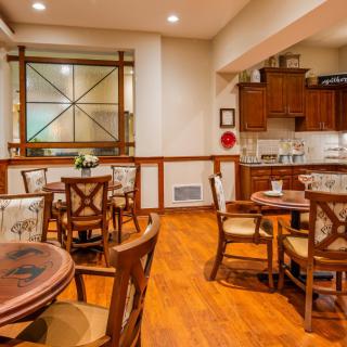A cozy dining area with wooden tables and chairs, adjacent to a well-lit kitchen.