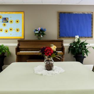 A cozy room featuring a piano, decorative flowers, and a simple table setting.