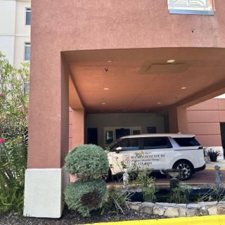 A hotel entrance with a vehicle parked under the carport surrounded by landscaping.