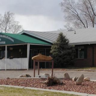A building with a green awning and sign, surrounded by trees and landscaping.