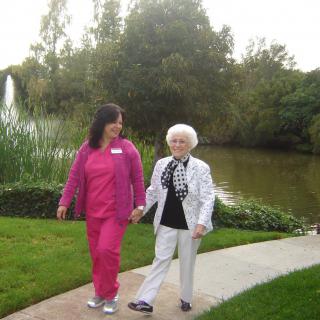 Two people walking together in a park beside a pond.