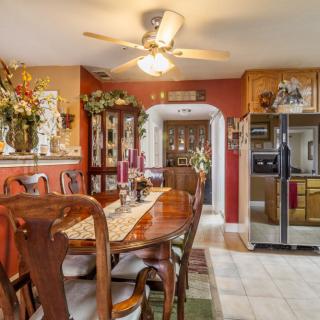 A cozy dining room with a traditional design, featuring a wooden table and chairs, ceiling fan, vibrant decor, and a view into the kitchen with stainless steel appliances.