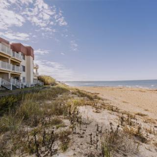 A serene view of a beachside residence with golden sand and a clear blue sky.