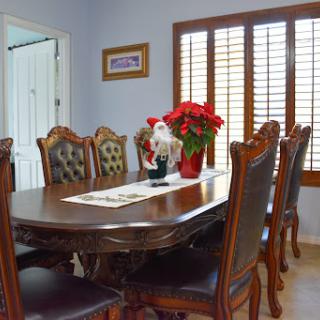 A beautifully arranged dining room featuring a wooden table surrounded by elegant chairs, complemented by decorative flowers and natural light from the windows.