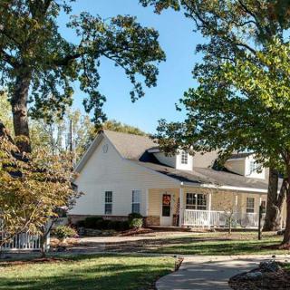 A charming house surrounded by trees and a well-maintained lawn on a sunny day.