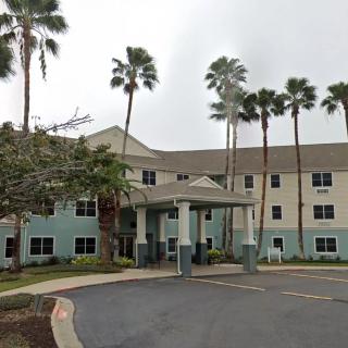 A three-story residential building with palm trees lining the entrance.
