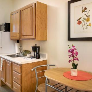 A cozy kitchen area with wooden cabinets, a small table with an orchid centerpiece, and framed artwork on the wall.