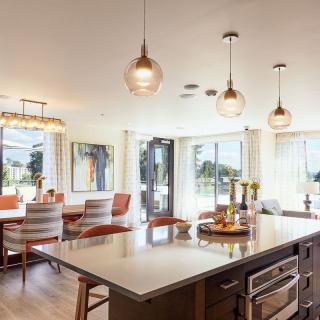 A modern kitchen and dining area featuring a central island with pendant lights, surrounded by large windows and stylish seating.