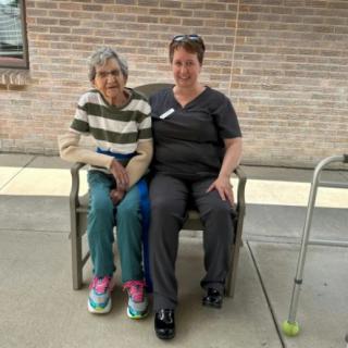 An elderly woman and a caregiver sitting together on a bench outside.