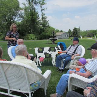 A group of people sitting in a circle outdoors, having a conversation in a garden setting.