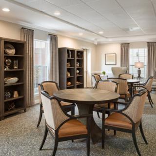 A cozy dining room with round tables, cushioned chairs, and decorative bookshelves.