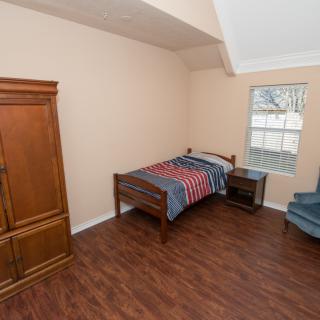 A simple bedroom with a single bed, wooden floor, and minimal furnishings.