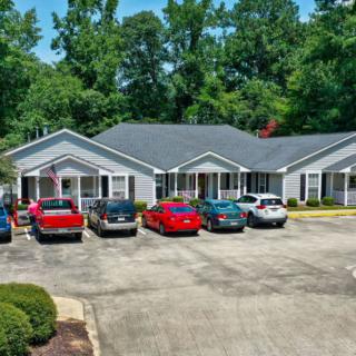 A small building with a parking lot in front and several cars parked, surrounded by trees.