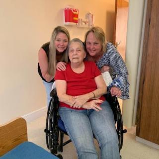 A heartwarming moment shared among three women, with one seated in a wheelchair and two standing beside her.