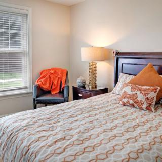 A cozy bedroom with a patterned bedspread and orange accents.