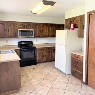 A kitchen with wooden cabinets, a stove, microwave, and refrigerator.