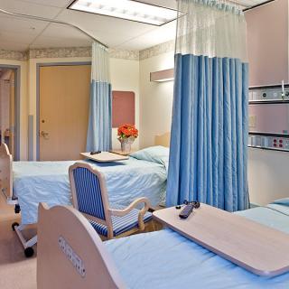 A clean and organized hospital room with multiple beds separated by curtains.