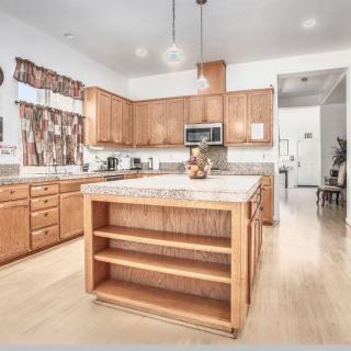 A modern kitchen with wooden cabinets and a central island, featuring bright lighting and appliances.