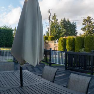 A tranquil patio setting with a table, chairs, and closed umbrella overlooking a fenced yard and trees.