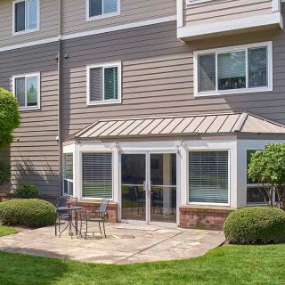 A modern house exterior with a patio, surrounded by greenery and equipped with outdoor furniture.