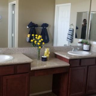 A bathroom featuring a double vanity with mirrors, decorated with yellow flowers and neatly hung towels.