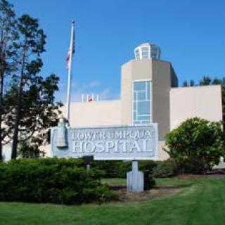 A hospital building with a prominent sign in front, surrounded by greenery and a clear blue sky.