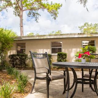 A serene outdoor patio area with a table, chairs, and surrounding greenery.