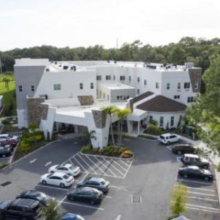 Aerial view of a large white building with an adjacent parking lot surrounded by trees.