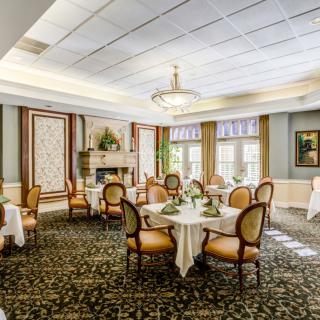 An elegantly designed dining room with round tables and upholstered chairs, featuring chandeliers and decorative carpeting.