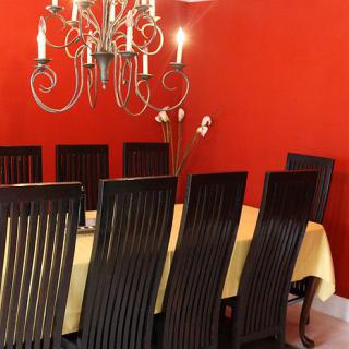 A dining room featuring a chandelier, red walls, and a set of dark wooden chairs around a table.