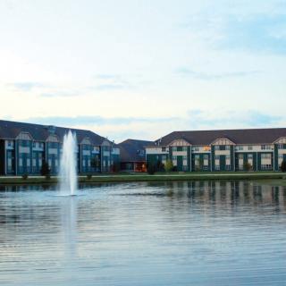 A serene view of buildings by a lake with a central fountain and reflections in the water.