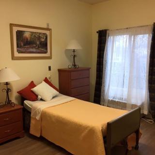 A cozy bedroom with a single bed, dresser, and warm lighting.