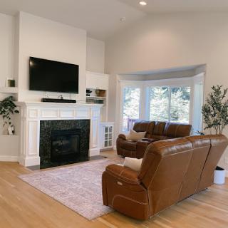 A cozy living room featuring a modern fireplace, comfortable brown leather couches, and ample natural light.