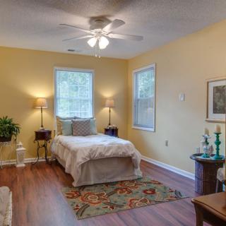 A cozy bedroom with warm yellow walls, featuring a single bed, wooden floors, and natural light streaming through the windows.