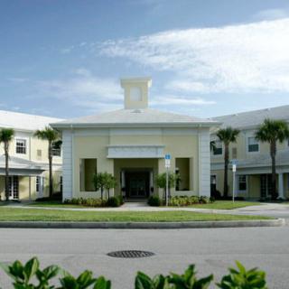 A modern building with palm trees and a central entrance under a clear sky.