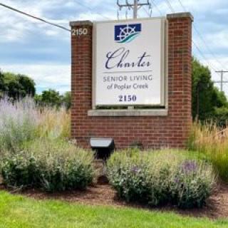 Outdoor sign for Charter Senior Living of Poplar Creek surrounded by greenery.