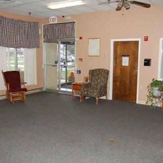 An empty waiting area with chairs, a carpeted floor, and windows with curtains.