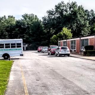 A school bus parked beside a row of vehicles on a calm day outside school buildings.