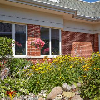 A beautifully landscaped garden surrounding a brick house with vibrant flowers.