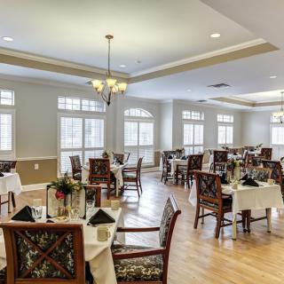 An elegant dining room with beautifully arranged tables and chairs, illuminated by natural light from large windows.