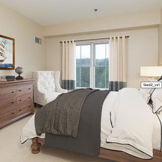 A cozy bedroom with a neatly made bed, wooden dresser, and a comfortable armchair by the window.
