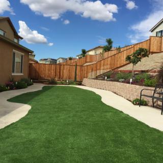 A well-maintained suburban backyard featuring artificial grass and a wooden fence.