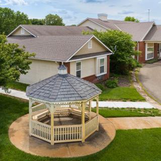 A peaceful outdoor setting with a wooden gazebo surrounded by houses and greenery.