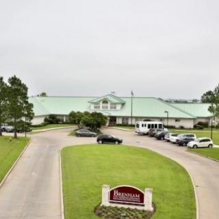 A large building with a green roof, surrounded by a parking lot and landscaped driveway.
