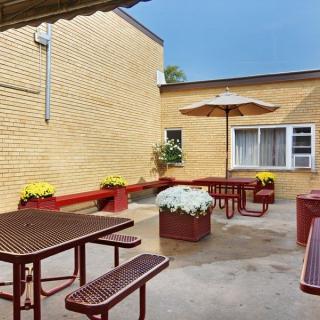 A cozy outdoor patio area with benches, tables, and vibrant flower arrangements against a brick building.