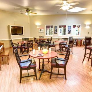 A cozy dining area with chairs and tables arranged neatly, featuring a wooden floor and overhead lighting.