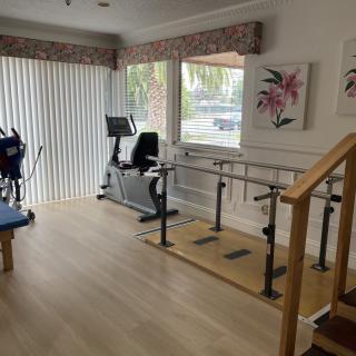 A rehabilitation room equipped with a stationary bike, parallettes, and stairs for physical therapy exercises.
