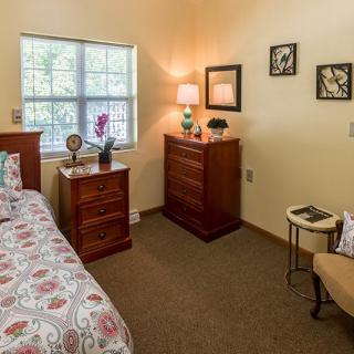 A cozy bedroom with a neatly made bed, wooden furniture, and soft lighting.
